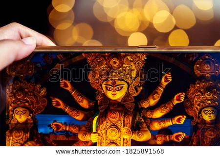 Hand holding mobile phone and taking photos of Goddess Durga idol at a pandal. Puja memories of 2019. The biggest religious festival of Hinduism and Bengali Community.