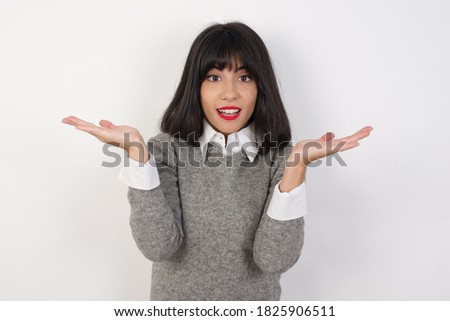 Surprised terrified Young businesswoman with retro short hairdo wearing casual clothes standing over isolated white background Gestures with uncertainty, stares at camera, puzzled as doesn't know 