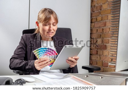 Young woman at work with a colorful palette in one hand and a tablet in the other, crying because she is overwhelmed with the task of choosing the right color