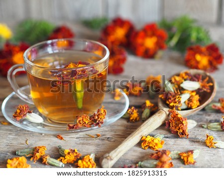Dried flowers of red flowers of calendula with a cup of medicinal tea on a wooden background. Herbal picking season.