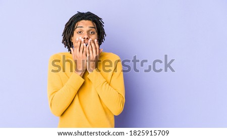 Young black man wearing rasta hairstyle shocked, covering mouth with hands, anxious to discover something new.