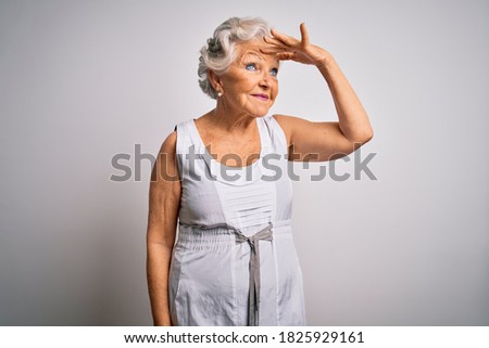 Senior beautiful grey-haired woman wearing casual summer dress over white background very happy and smiling looking far away with hand over head. Searching concept.