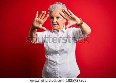Senior beautiful woman wearing elegant shirt standing over isolated red background doing frame using hands palms and fingers, camera perspective