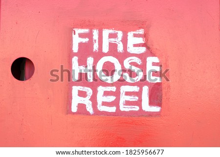 Inscription by white paint Fire Hose Reel on a red wall.