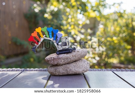 small metal model of  toy excavator on two large stones. Bright pins in rainbow colors are pinned to boom of excavator. business - congratulations for construction company. Builder's Day.