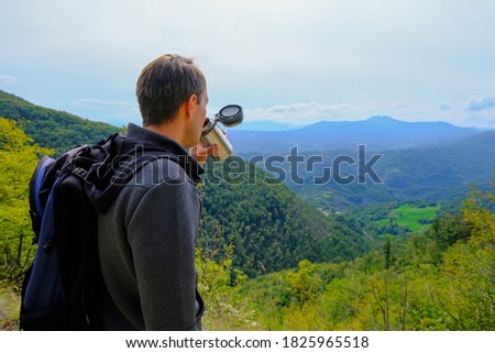 Man, hiker drinking beverage from a thermos in the mountains. Traveler with backpack. Natural background. Copy space. High quality photo