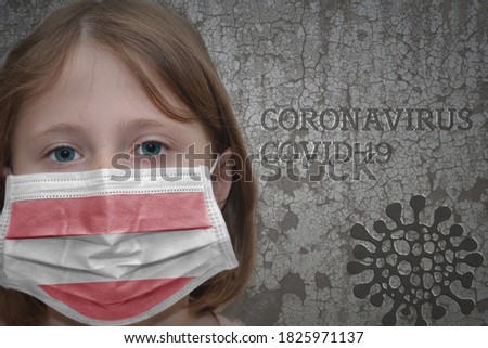 Little girl in medical mask with flag of austria stands near the old vintage wall with text coronavirus, covid, and virus picture.