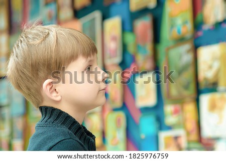 The boy looks at the paintings at the exhibition of pictorial art and creativity.