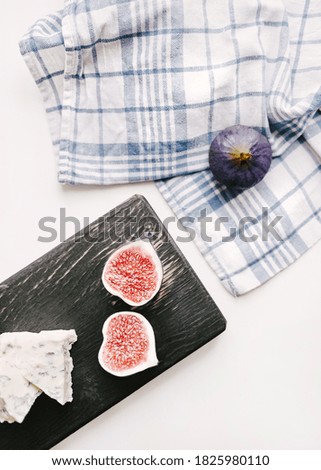 Figs and blue cheese Top view photo Fruits and cheese on dark wooden plate with checkered napkin on white backdrop