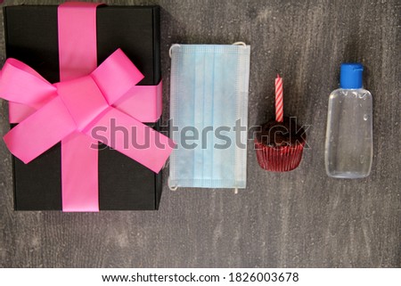 
overhead view of gift and birthday cake with protection mask and antibacterial gel, new normal covid-19 on vintage gray wooden background