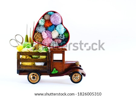 Heart-shaped box with multicolored  skeins of yarn for knitting and hooks  in the wooden toy car on the white background. Crochet and knitting. Women's working space.
