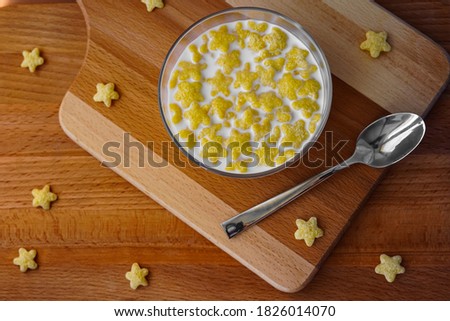 On a wooden table is a cutting board, on top is a glass plate with cereal and milk. A metal spoon lies nearby. Tasty breakfast - wholesome food - proper nutrition. Photo taken from top view
