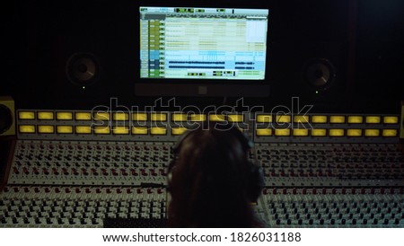 Unrecognizable sound engineer working in music studio. Rear view of man touching soundboard indoor. Unknown male musician adjusting sound in recording studio.