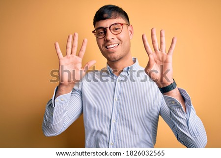 Young handsome hispanic business man wearing nerd glasses over yellow background showing and pointing up with fingers number nine while smiling confident and happy.