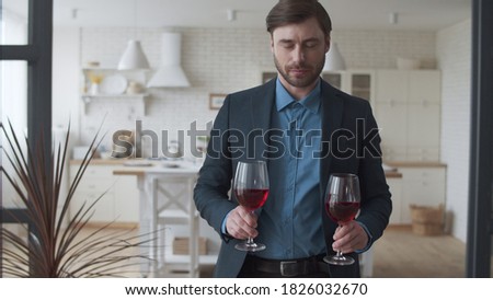 Attractive family couple drinking red wine at home together. Smiling man bringing glasses with wine to woman. Happy family celebrating success with alcohol drink on couch in slow motion.