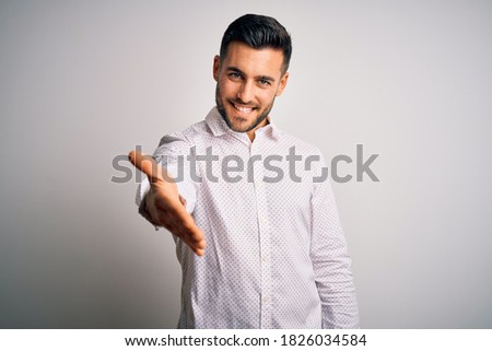 Young handsome man wearing elegant shirt standing over isolated white background smiling cheerful offering palm hand giving assistance and acceptance.