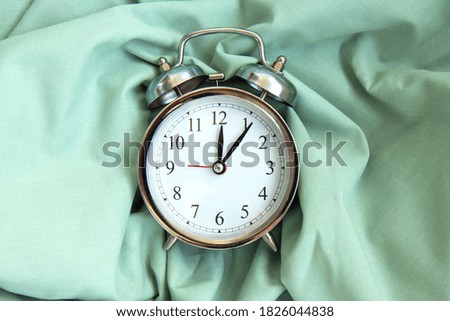 Beautiful vintage silver alarm clock on the folds of green natural fabric background with shadows. Time concept. Holiday routine