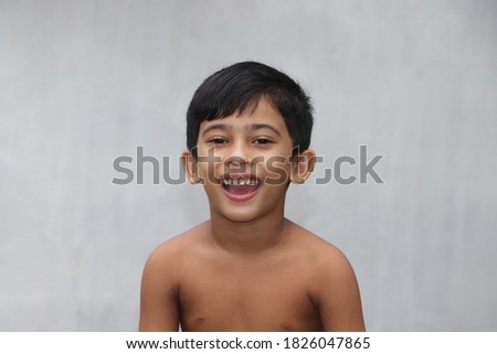 Cute little bare chested Asian boy smiling and expressing much happiness in the face. Happy healthy child posing for photo isolated on gray background