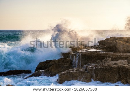 Big wave crashes against the rocks of a coast in the sunlight Royalty-Free Stock Photo #1826057588