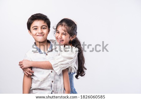 Cute little Indian asian siblings standing and embracing each other in white clothes while standing againstwhite background. Royalty-Free Stock Photo #1826060585