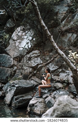A young Caucasian female sitting on a rock near a river and taking photos
