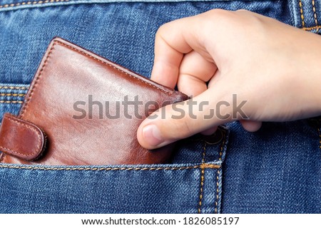 A hand pulls a wallet out of the back pocket of his jeans.The concept of pickpocketing or theft in the family from parents. Royalty-Free Stock Photo #1826085197