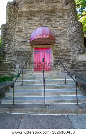 Steps Leading Up to a Red Door on a Cobblestone Church With a Welcome Sign Above It
