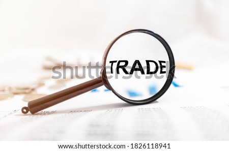 TRADE word through Magnifying glass on office table, charts and money.