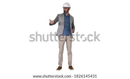 Architect man in helmet and head set talking to camera and making gestures showing on some objects on white background.