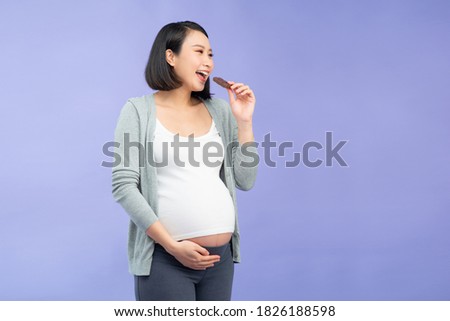 Portrait of happy pregnant woman with chocolate bar standing over purple