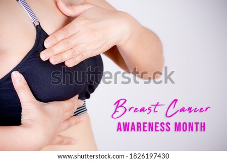 Woman hand checking lumps on her breast for signs of breast cancer on gray background with text Breast cancer awareness month.