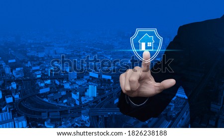 Businessman pressing house with shield flat icon over modern city tower, street, expressway and skyscraper, Business home insurance and security concept