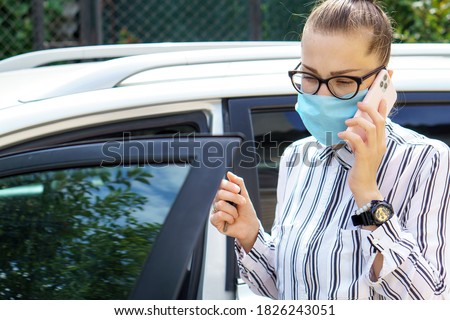 beautiful successful prosperous rich business woman in white suit talking on phone wearing a medical mask standing near the car salon. allergy, coronavirus, lady style, quarantine, pandemic concepts.