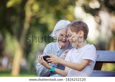 Young boy and his great grandmother using smartphone to makie video call or take selfie. Streaming online video call. Mobile internet. Watching video on smartphone. Royalty-Free Stock Photo #1826252120