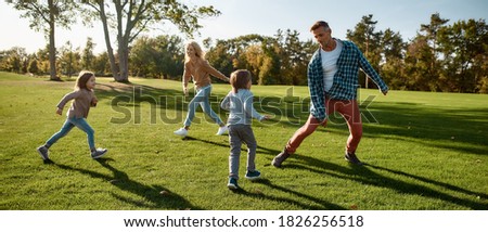 Full-length portrait of happy mother, father, little boy and girl running and playing catch game in autumn park. Family, parenthood, leisure and people concept. Horizontal shot.
