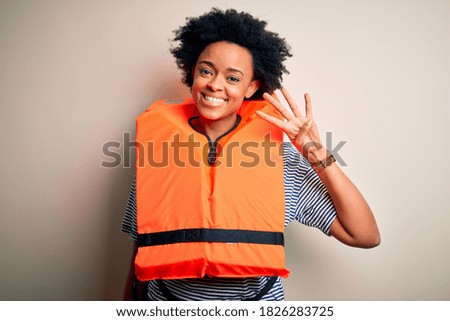 Young African American afro woman with curly hair wearing orange protection lifejacket showing and pointing up with fingers number four while smiling confident and happy.
