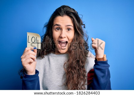 Young beautiful woman with curly hair holding reminder paper with lol message screaming proud and celebrating victory and success very excited, cheering emotion Royalty-Free Stock Photo #1826284403