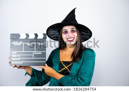 Woman wearing witch costume over isolated white background holding clapperboard very happy having fun