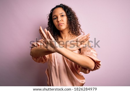Young beautiful woman with curly hair wearing casual t-shirt standing over pink background Rejection expression crossing arms doing negative sign, angry face