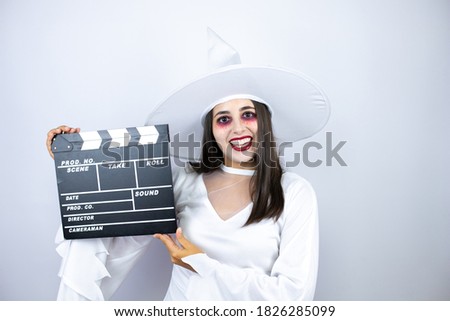 Woman wearing witch costume over isolated white background holding clapperboard very happy having fun