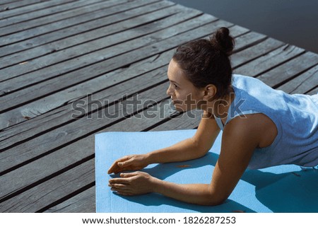 The young woman does a plank exercise on a gymnastic mat and looks in front of her. Side view. Meditation, yoga in nature.