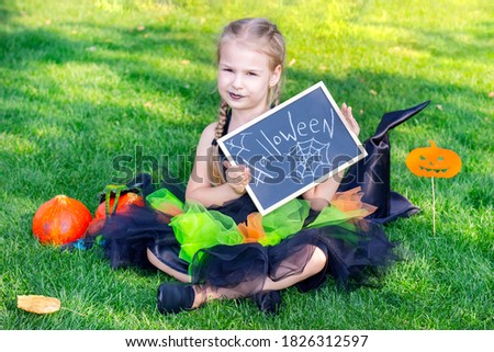 girl in a witch costume for the Halloween holiday. Placard with the inscription: Halloween. Girl sitting on the grass