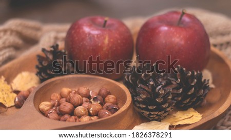 Autumn still life with apples and nuts. Autumn background with apples on a warm knitted scarf, a wooden plate, autumn leaves, hazelnuts and cones.