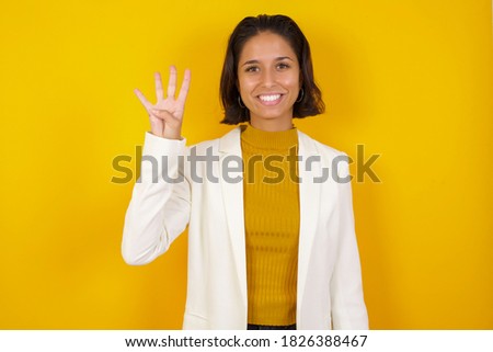 Young businesswoman standing against yellow wall showing and pointing up with fingers number four while smiling confident and happy.