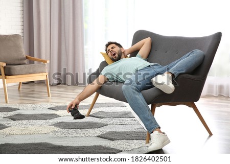 Lazy young man playing video game while lying on sofa at home Royalty-Free Stock Photo #1826402501