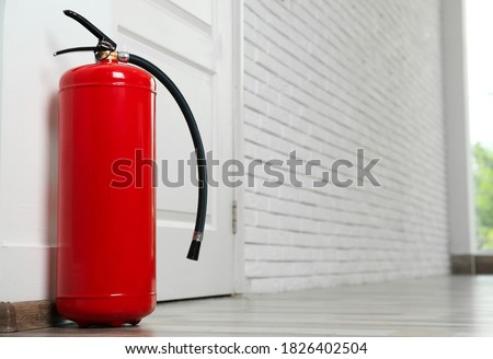Fire extinguisher on floor near door indoors, space for text
