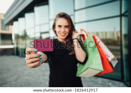 Portrait of european lady hold hand colorful bags woman after shopping in black dress plastic credit card retail store near mall on the street sunshine sales black friday season bokeh background 
