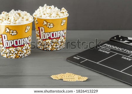 A closeup shot of popcorn buckets next to a clapperboard and cinema tickets on a gray background