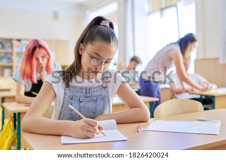 Lesson in class of teenage children, in front girl 13, 14 years old sitting at desk writing in notebook. Education, school, college, schoolchildren concept Royalty-Free Stock Photo #1826420024