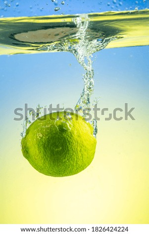 Whole green lime drops under water with splashes on gradient background